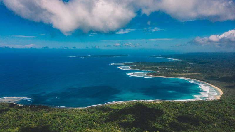 Teluk panjang berair biru toska dan bukit hijau dilihat dari atas